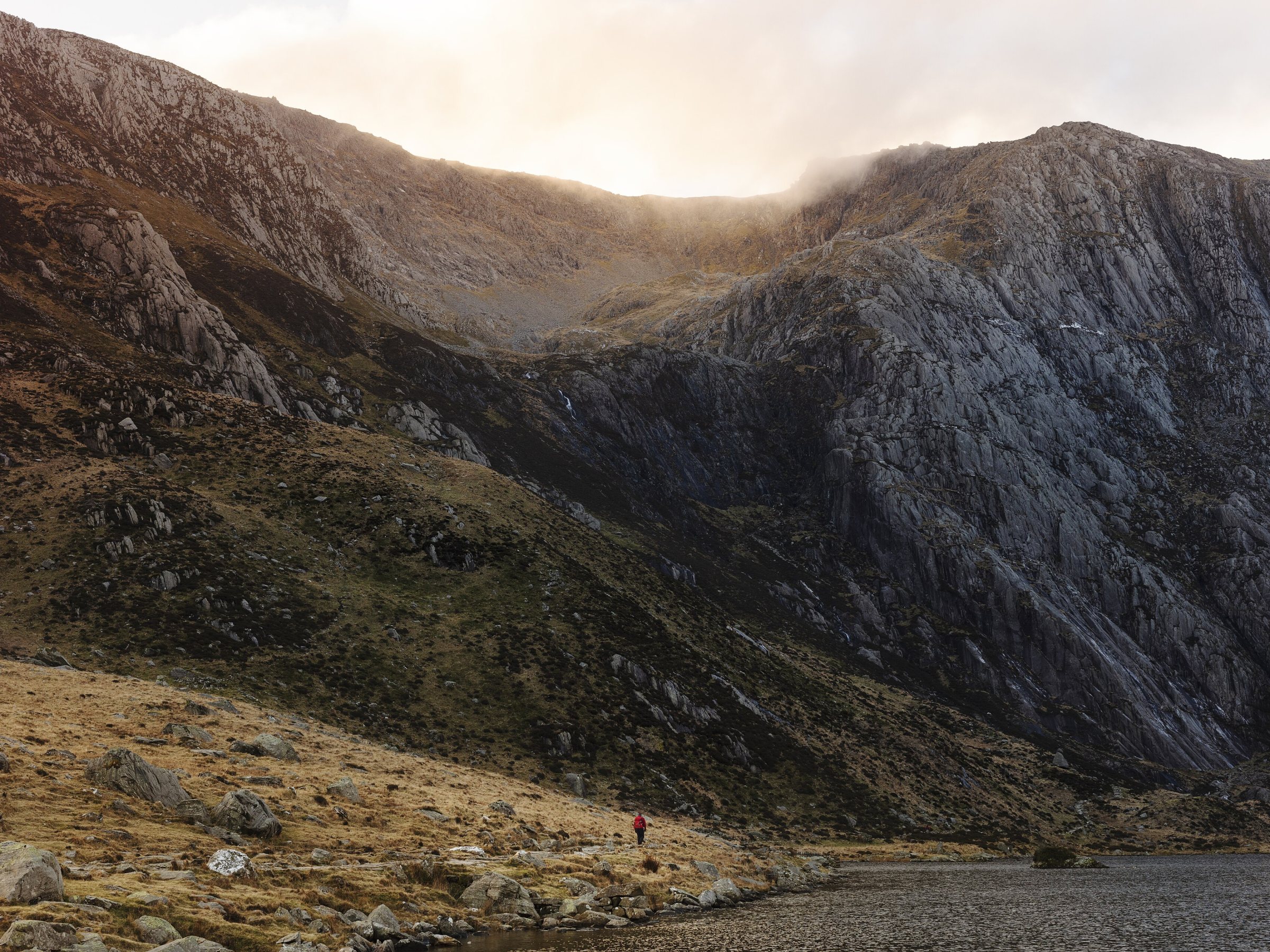 A walker beside Llyn Idwal beneath the Idwal Slabs in Cwm Idwal, Eryri