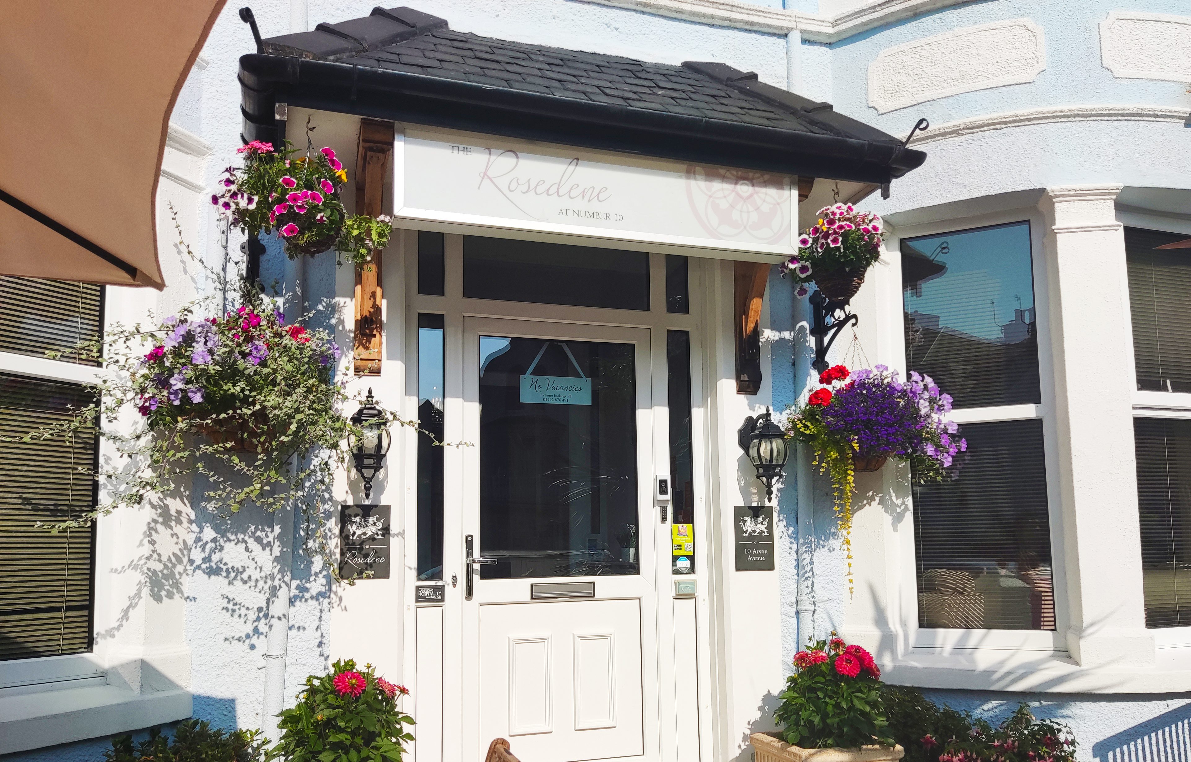 The front door of The Rosedene on Arvon Avenue, Llandudno, with hanging baskets either side